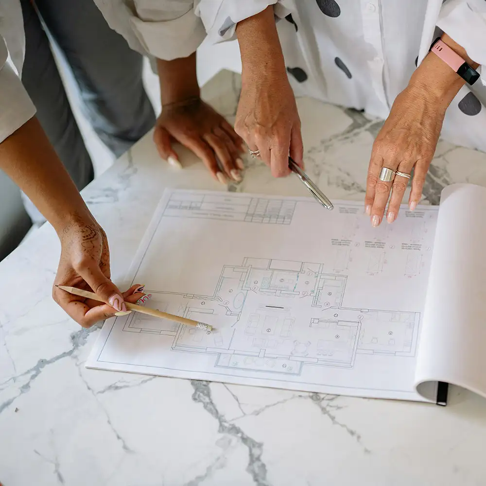 Two people reviewing architectural plans on a marble table, pointing with a pencil and a pen.
